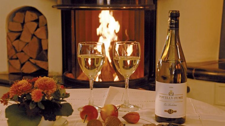 Une table cozy avec deux verres à vin, une bouteille de champagne et des pommes fraîches. À l'arrière-plan, une cheminée brûle et crée une atmosphère chaleureuse.