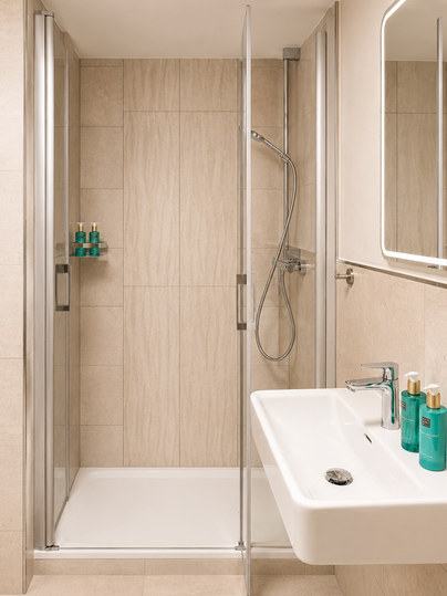 Een modern badkamer met een glazen douche en een eenvoudig wastafel. De muren zijn in neutrale kleuren gehouden, en enkele verzorgingsproducten staan klaar.