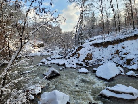 A picturesque river flows through a winter landscape with snow-covered trees and rocks. The serene scene radiates a peaceful atmosphere.