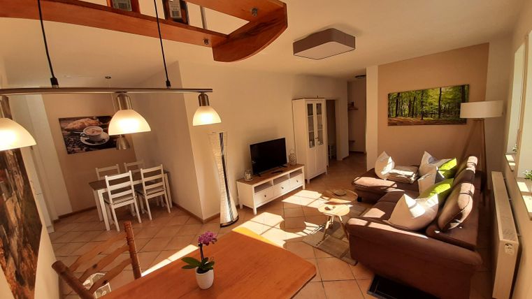 Ein gemütliches Wohnzimmer mit einem Essbereich und einem großen Fenster. Die Einrichtung ist modern und hell, mit bequemen Sofas und einem Esstisch.