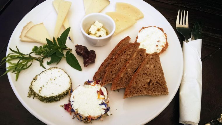 Een bord met verschillende soorten kaas, vers brood en kruiden. Daarnaast bevindt zich een klein schaaltje met feta-kaas.