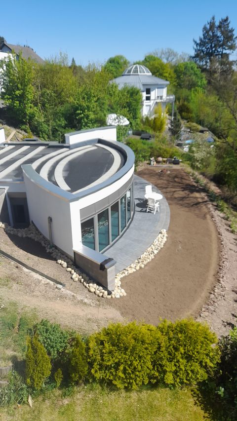 Une maison moderne à la façade incurvée et dotée de grandes fenêtres. Entourée d'un paysage verdoyant et d'un jardin aménagé.