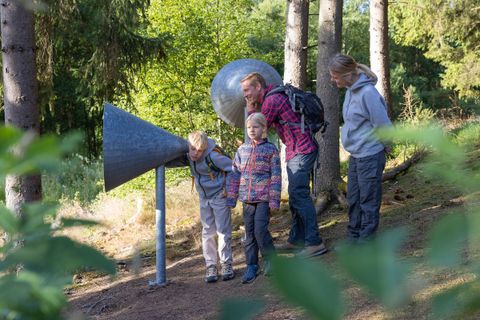 Eine Familie an einer Hörstation auf dem Walderlebnisparcours Kölschkier