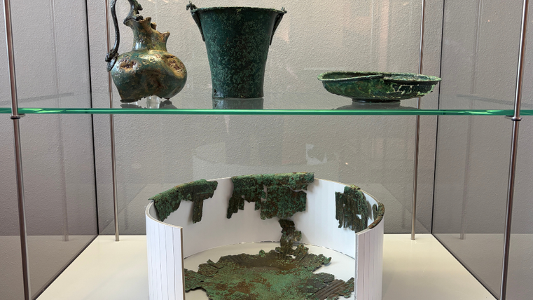 In einer Vitrine stehen mehrere große Bronzegefäße, die grün verfärbt sind.