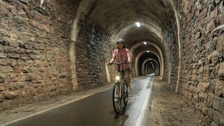 Person fährt mit Fahrrad durch einen beleuchteten Tunnel mit Steinwänden.