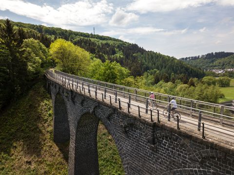 Two cyclists on a viaduct in the countryside.