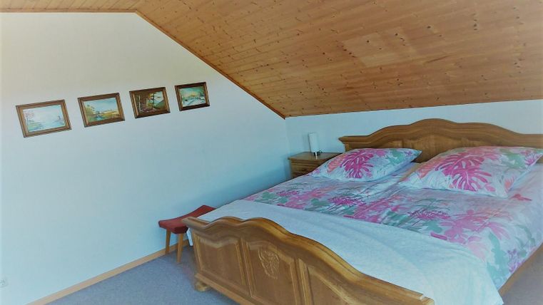 Een gezellige slaapkamer met houten meubels en een tweepersoonsbed. Aan de muur hangen schilderijen, en het plafond is schuin.