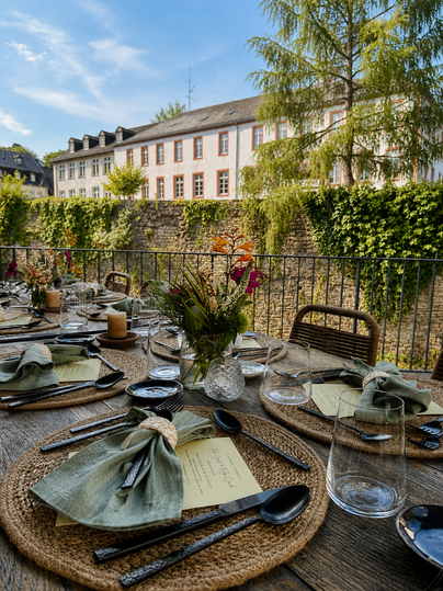 Une belle table dressée à l'extérieur avec vue sur un bâtiment historique. La décoration de la table comprend des serviettes vertes, de jolies fleurs et des verres élégants.