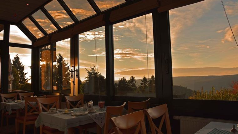 Ein gemütliches Restaurant mit großen Fenstern und Blick auf die Landschaft. Die goldene Abenddämmerung lässt den Raum warm erstrahlen.