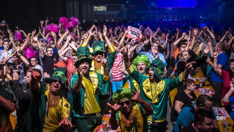 Eine lebhafte Menschenmenge feiert mit fröhlicher Stimmung. Einige Personen tragen bunte Kostüme und jubeln.