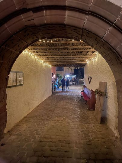 Ein einladender Durchgang mit Steinboden und warmem Licht. Im Hintergrund sind Menschen zu sehen, die sich unterhalten.