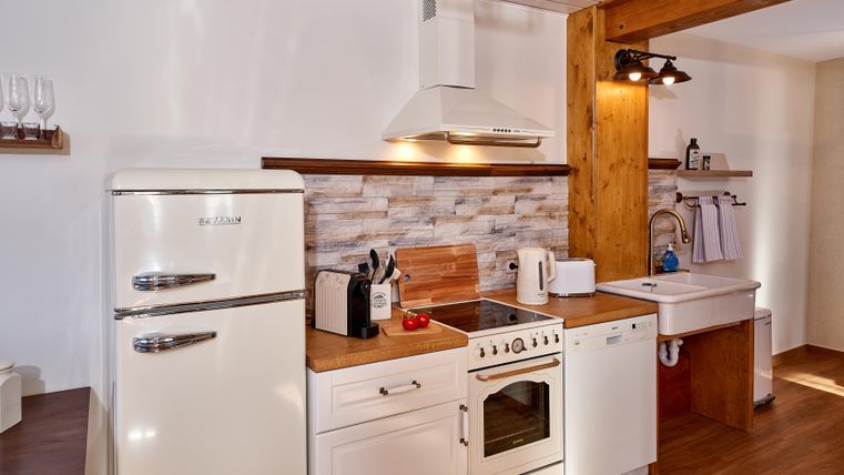 Eine moderne Küche mit Holzregalen und weißen Schränken. Sie ist mit einem Kühlschrank, einem Herd und einer Spüle ausgestattet.