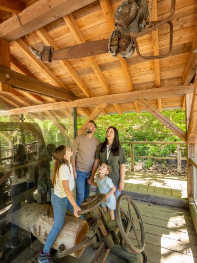 Eine Familie besichtigt eine alte Maschine in einem historischen Gebäude. Sie schauen neugierig nach oben zu einem historischen Werkzeug, das an der Decke hängt.