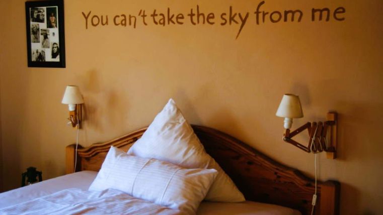 A cozy bedroom with a large bed and decorative pillows. On the wall is the saying: "You can't take the sky from me."