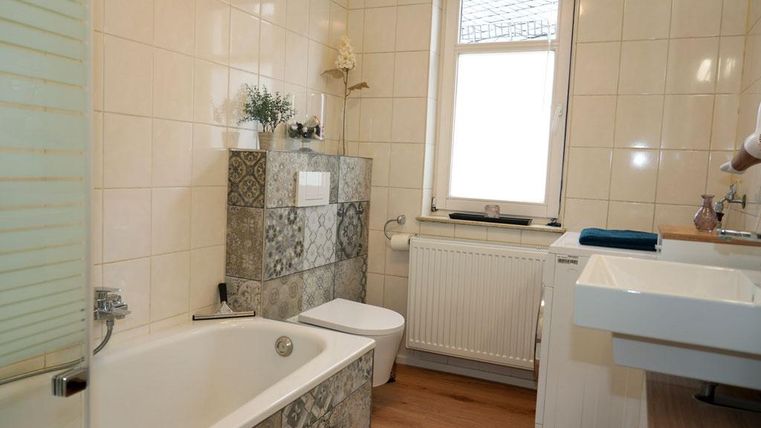 A modern bathroom with a bathtub and a sink. The elegant tiles and the wooden design create an appealing atmosphere. A washer-dryer is available to you.
