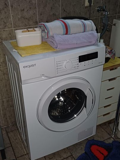 Une machine à laver est dans une salle de bain.
Des serviettes y sont soigneusement disposées et les murs sont carrelés.