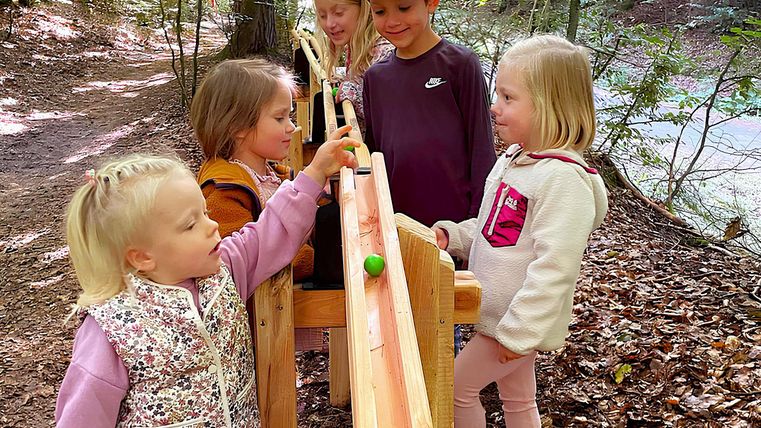 Groupe d'enfants mélangé de filles et de garçons fait rouler une boule sur la piste en bois