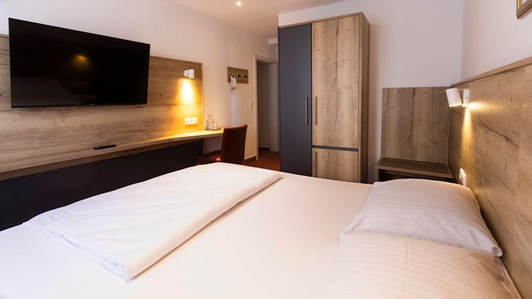 A modern hotel room with a double bed and a flat-screen TV. The room is bright and friendly with wooden details and a desk.