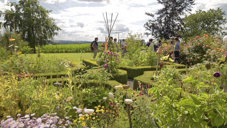 A beautiful garden with colorful flowers and an artistically designed boxwood maze. In the background, people can be seen enjoying nature.
