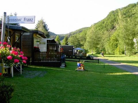 Un beau camping avec des cabanes en bois et beaucoup d'herbe verte. Entouré de collines boisées et de fleurs en fleurs.