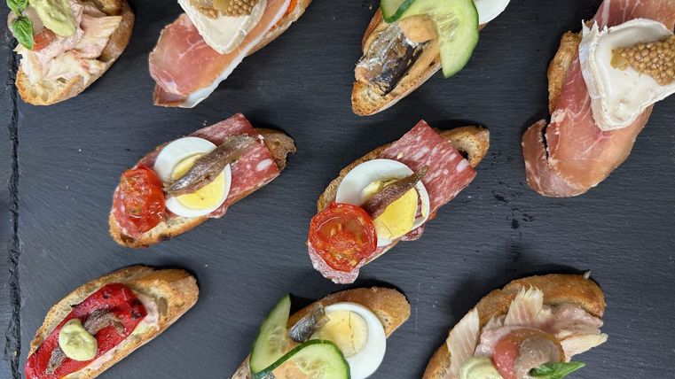 Eine Auswahl an köstlichen Canapés auf einem schwarzen Steinbrett. Die Canapés sind mit verschiedenen Belägen wie Schinken, Eiern, Gemüse und Soßen dekoriert.