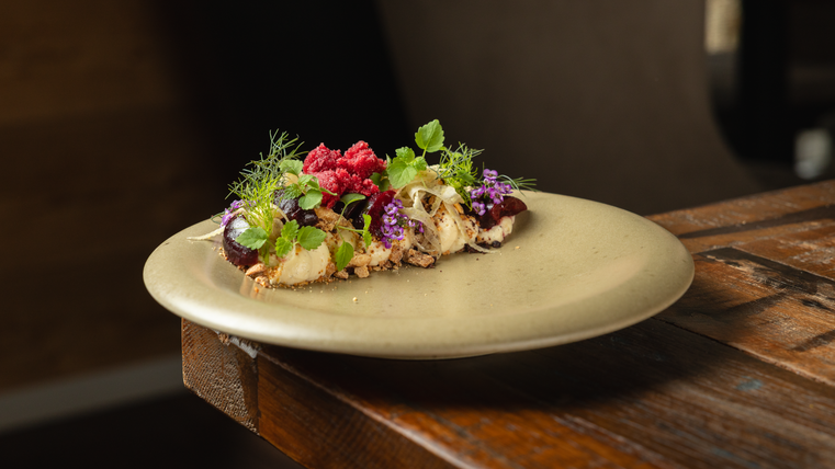 Une assiette artistiquement dressée avec différentes herbes et baies. Le plat a l'air frais et appétissant.