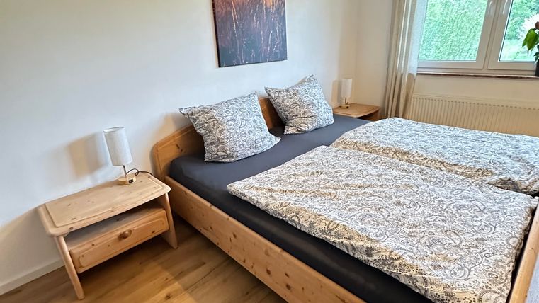 Ein gemütliches Schlafzimmer mit einem großen Bett und hellen Holzmöbeln. An der Wand hängt ein Bild einer Landschaft, und das Zimmer hat viel Tageslicht.