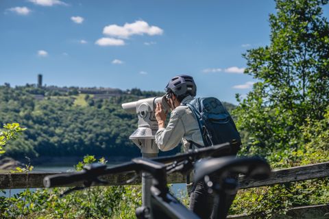 Persoon met helm kijkt door een verrekijker in een vogelobservatiepost, Vogelsang IP op de achtergrond.
