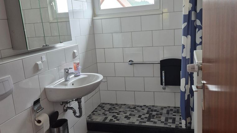Een moderne badkamer met witte tegels en een grote spiegel. De douche is uitgerust met een blauwe douchegordijn en een matzwarte vloer.