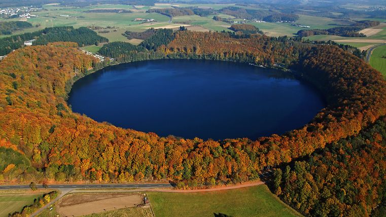 Luftaufnahme des Pulvermaars, umgeben von herbstlich gefärbtem Wald.