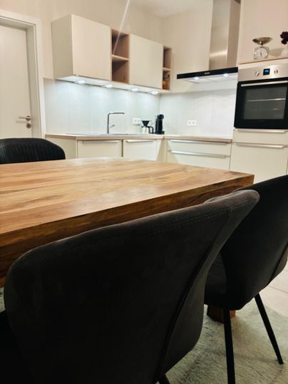 Een moderne keuken met witte meubels en een houten stamtafel. Op de achtergrond zijn keukenapparaten en lichtbronnen zichtbaar.