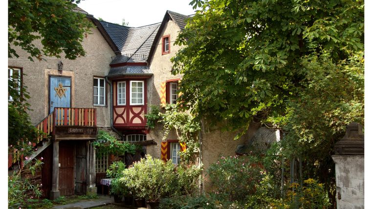 Een charmant huis met een kleurrijke gevel en een balkon. De tuin is weelderig en omgeven door bomen.
