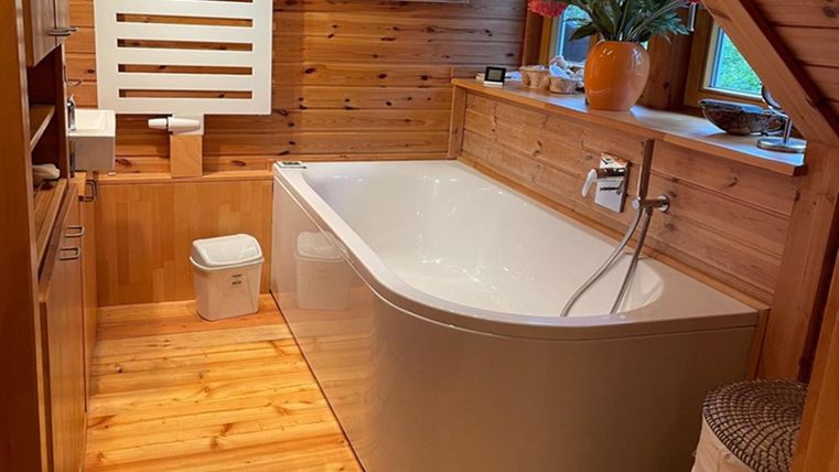 A modern bathroom with a freestanding bathtub and wooden cladding. The decor is bright and inviting, with plants and natural light.