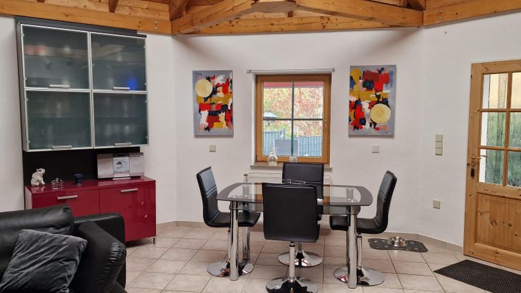 Un salon moderne avec une table à manger et des chaises noires. Des images colorées sont accrochées aux murs et une fenêtre laisse entrer beaucoup de lumière naturelle.