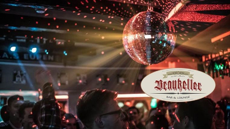 A lively bar with dancing people and a glittering disco ball. Colorful lights create a festive atmosphere.