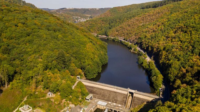 Aerial view of a reservoir with surrounding wooded hills and a dam wall.