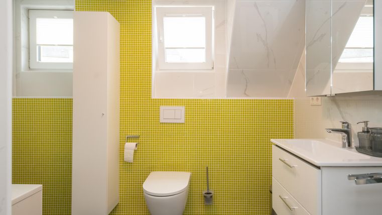 Ein modernes Badezimmer mit gelben Fliesen und weißen Möbeln. Es gibt ein Fenster und eine Dusche.