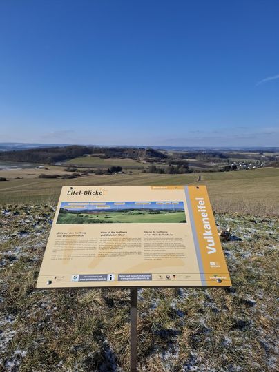 Une table d'observation se trouve sur une colline surplombant un vaste paysage. Le ciel est clair et bleu, et les environs sont verts et doucement vallonnés.