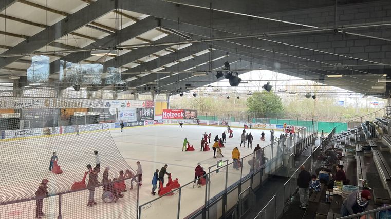 Une patinoire avec beaucoup de gens qui sont sur la glace. Certaines personnes sont assises sur un banc et observent la scène.
