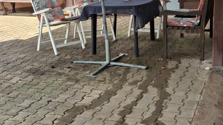 A cozy outdoor area with a table and chairs under a large sunshade. The floor is made of stone slabs and there is a calm atmosphere.