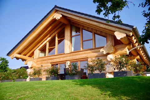 Une maison en rondins moderne avec de grandes fenêtres dans un jardin clôturé. L'architecture allie des éléments traditionnels et contemporains.
