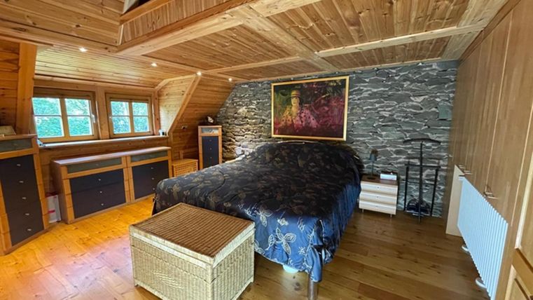 A cozy bedroom with wooden paneling. There is a large bed, a wicker table, and a piece of artwork on the wall.