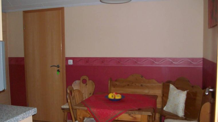 Een gezellige eetruimte met houten meubels en een rode tafellaken. Op de tafel ligt een fruitschaal en de muren zijn in zachte kleuren geschilderd.