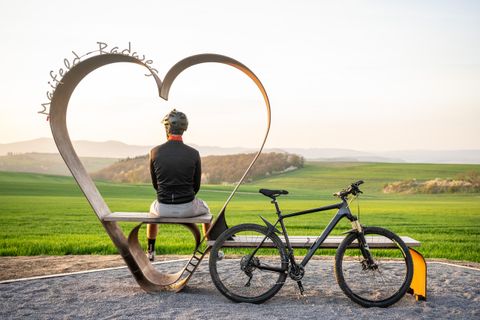 The photo shows a cyclist from behind on the treasure bench in heart shape.