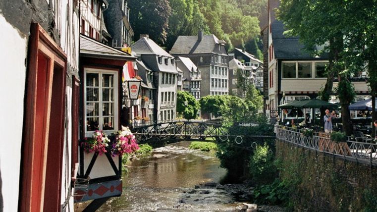 Une ville pittoresque au bord de la rivière avec des maisons décorées de manière festive et des arbres verts. Des ponts relient les bâtiments et créent une atmosphère accueillante.
