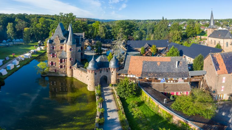 Luftaufnahme von Burg Satzvey mit Wassergraben und umliegenden Gebäuden.