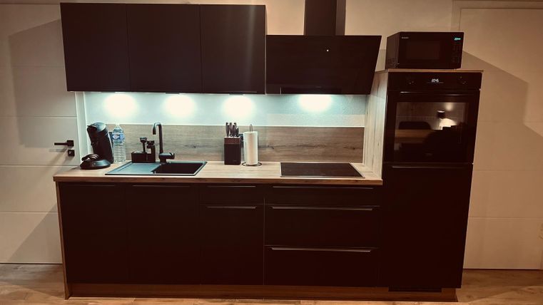 Une cuisine moderne avec des armoires sombres et un plan de travail clair. Elle est équipée d'une plaque de cuisson, d'un évier et de nombreux appareils de cuisine.