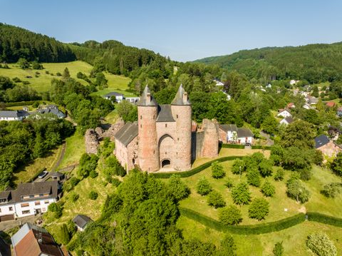 Vue aérienne du château de Bertrada à Mürlenbach, entouré d'un paysage verdoyant et de maisons.