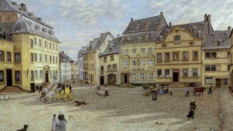 Eine historische Stadtansicht mit bunten Gebäuden und einem großen Platz. Menschen und Tiere beleben die Szenerie.