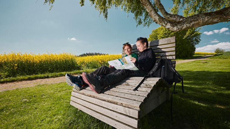 Deux femmes se détendent sur une chaise longue en bois tout en regardant une carte de randonnée.